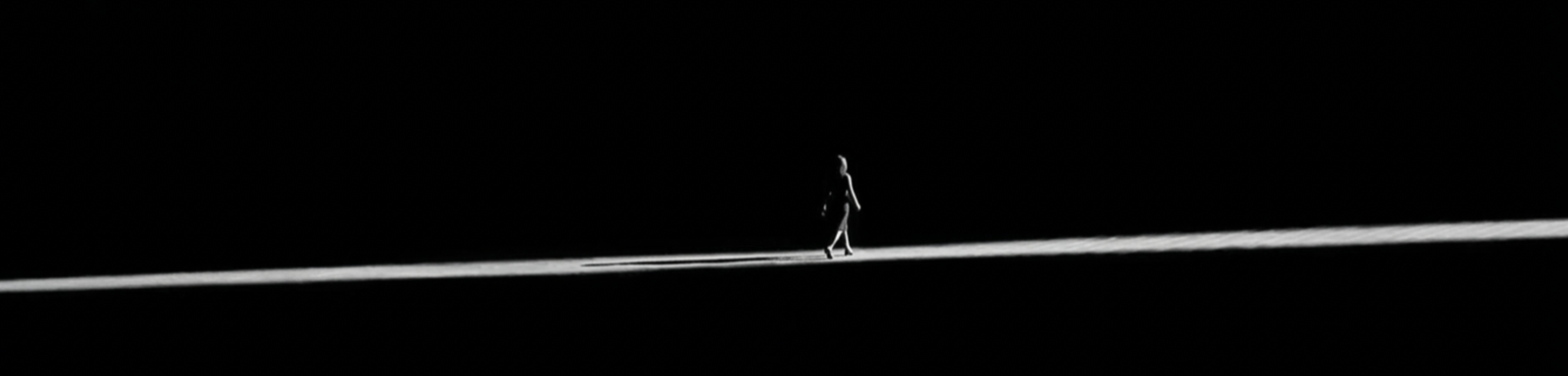 A lone figure walking along a thin line of light in total darkness